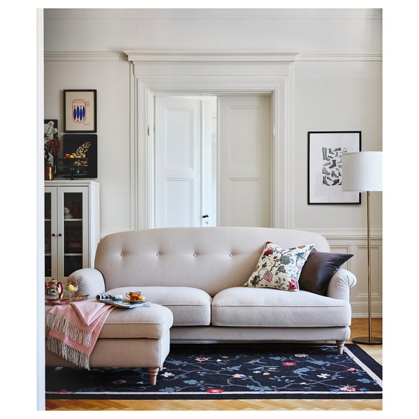 Beige ESSEBODA sofa with floral rug, pillows, and decor; open door.