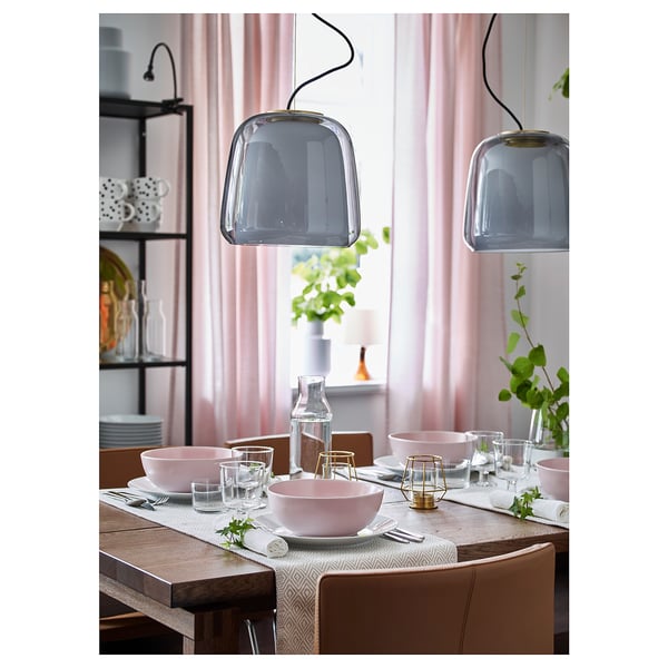 Modern dining area with two smoky glass pendant lamps, light pink tableware, and wooden chairs.