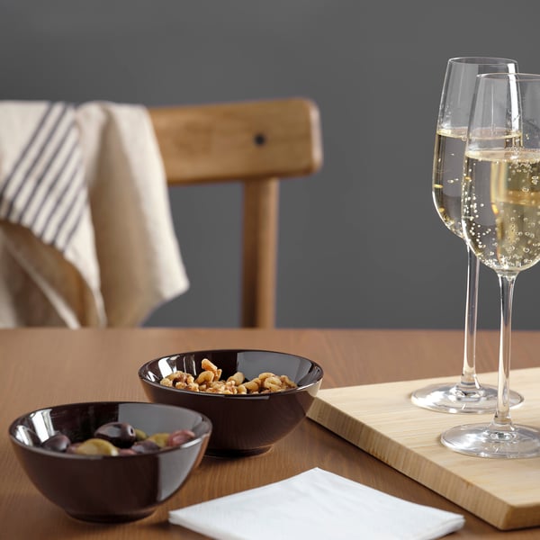 Two dark bowls, one with nuts, one with olives. Two wine glasses, a napkin, on a wooden table.