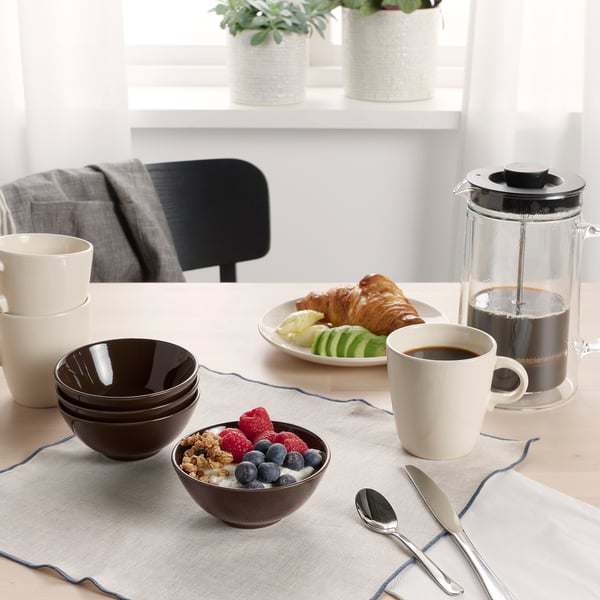 Table set with FÄRGKLAR bowls and mugs, featuring breakfast items like granola, berries, croissants, and a cafetière with coffee.
