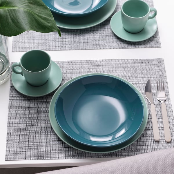 Table setting with two place mats, each with a green mug, saucer, deep plate, and cutlery.