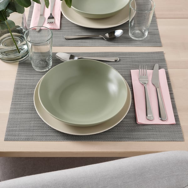 Table set with green bowl, white plate, utensils, glass, and napkin on placemat.