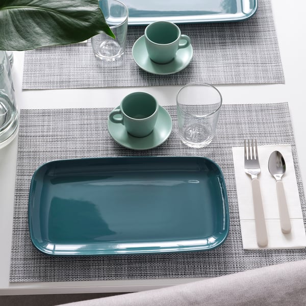 Two place settings with grey placemats, teal dinnerware, cups, glasses, utensils, and a tray.