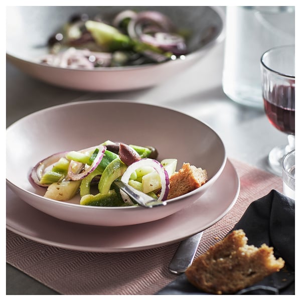 A dish set with FÄRGKLAR pink plates, filled with salad. Sliced bread and drinks are also present.