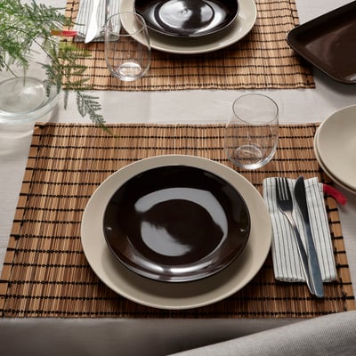 Bamboo placemat with brown and beige plates, cutlery, and glasses.