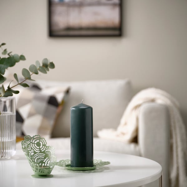 FENOMEN dark green pillar candle on a white table. Tall, single cylindrical shape. Placed near small decorative green items, creating cosy atmosphere.