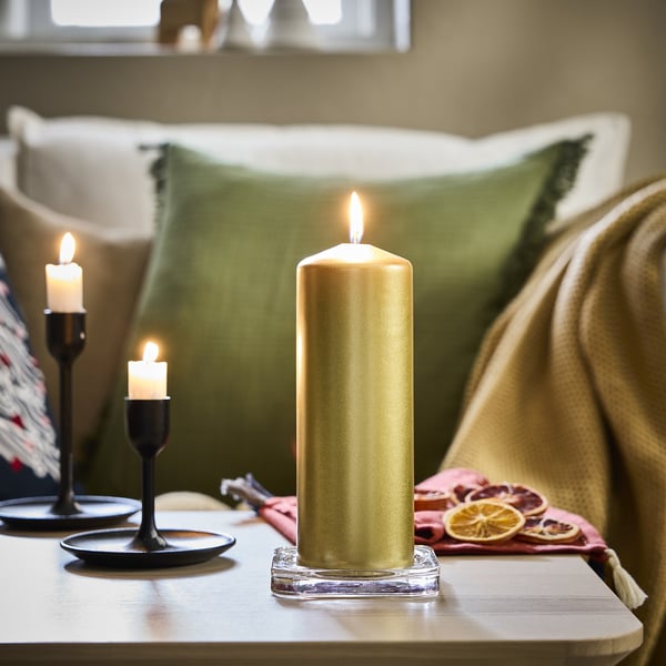 Gold candles on table, one tall, two small. Green pillows, cosy blanket.