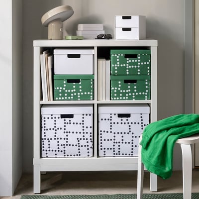 A kallax shelf with six FJÄDERHARV boxes and items on top, including a lamp and a green towel hanging on the right side.