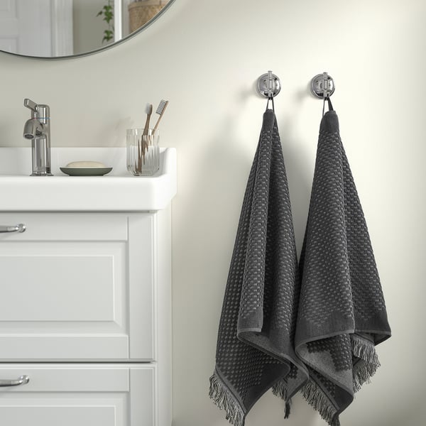 FJÄLLSTARR dark grey towels with fringes on wall hooks, next to sink and mirror.