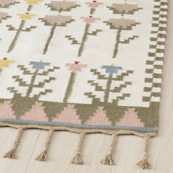 Handwoven rug with intricate midsummer patterns, featuring braided edges and vibrant wool colours, showcasing high-quality craftsmanship.