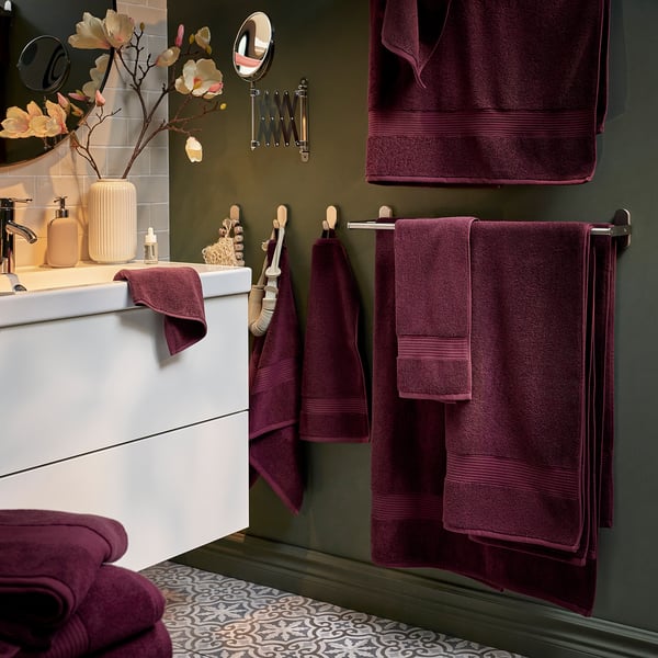 Modern dark green bathroom with white vanity, maroon towels, flowers.