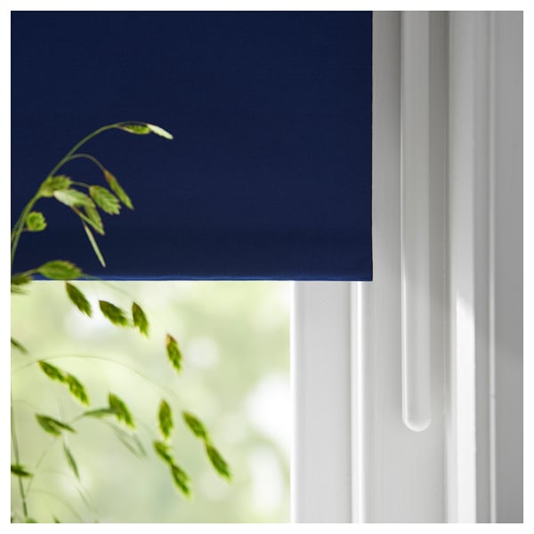 A navy blue FRIDANS roller blind partially drawn, with green plant leaves visible through the window.