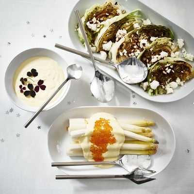 Three dishes of gourmet salad and sauces arranged on a decorative tablecloth, served with stainless steel serving utensils.