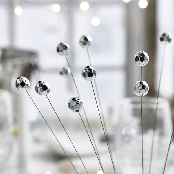 Silver spherical ornaments on thin rods, reflecting light, mounted on a shiny base. Appears festive and well-crafted.
