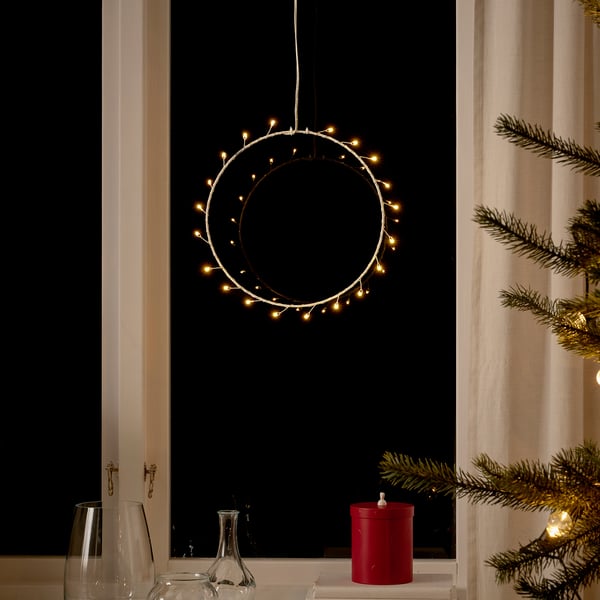 Festive window with large warm circular light decoration, vases, candle holder, and pine branches.