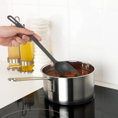 Hand stirring saucepan with grey spoon; capability of non-stick coating care.