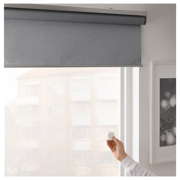Hand holding remote controls smart roller blind, adjusting window light.