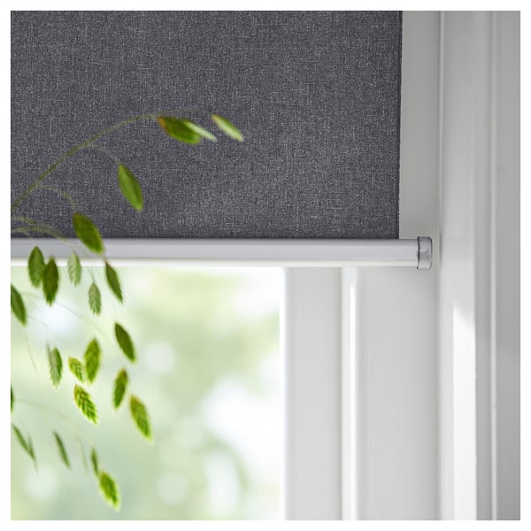 Roller blind, grey colour, cordless design, mounted on white window frame, partial view of green plant.