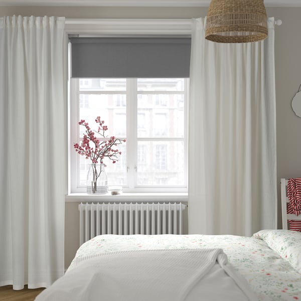 Modern bedroom with grey roller blinds, curtains, floral bed quilt, and pink flowers.
