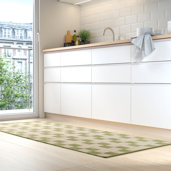 A modern kitchen with a white counter, GÅNGSTIG mat, and some items on it, near a window showing a building outside.