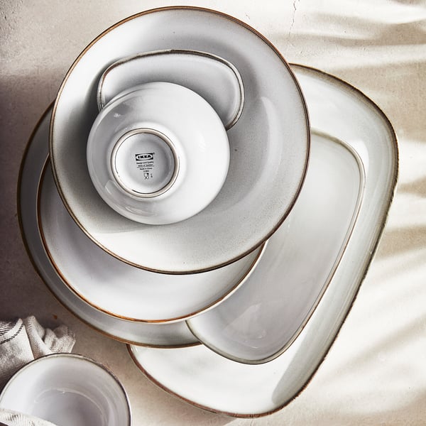 Stacked white stoneware plates, round and rectangular, with sandy glaze and golden rim, GLADELIG series, IKEA.