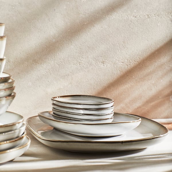 A stack of light grey, stoneware plates with a textured glaze and slightly irregular shape, arranged neatly for a table setting.