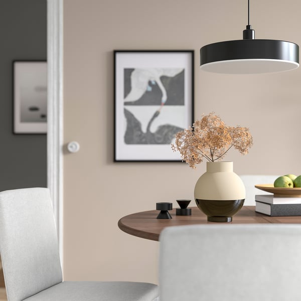 Modern dining table with black & beige vase, dried flowers, small candle holders, green apples, pendant light, & abstract wall art.