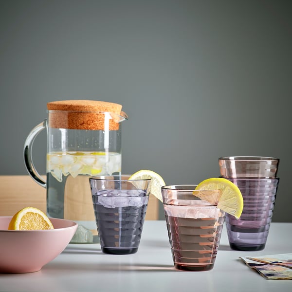 Three purple glasses with lemon slices sit next to a pitcher with ice and water.