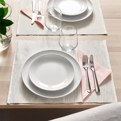 Two table settings with white plates, cutlery, glasses, and cloth napkins on placemats on a wooden table.