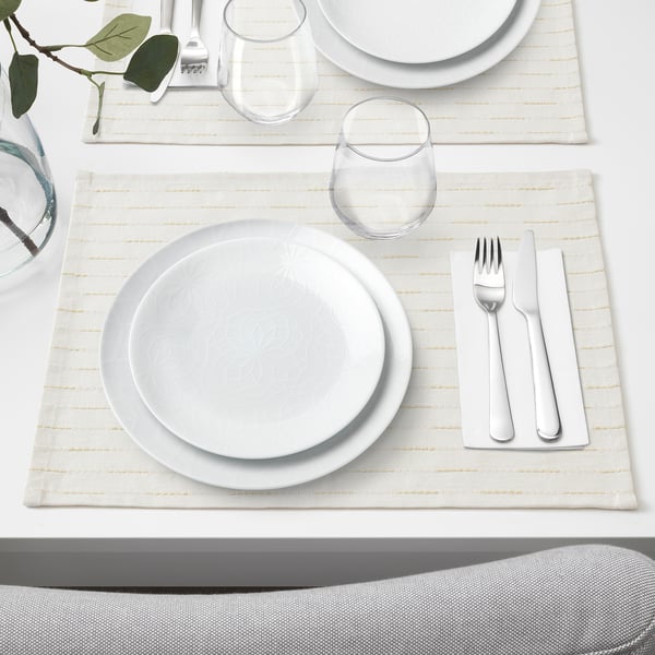 Elegant place setting with white plate, glass, and silverware on beige mat, ready for dining.