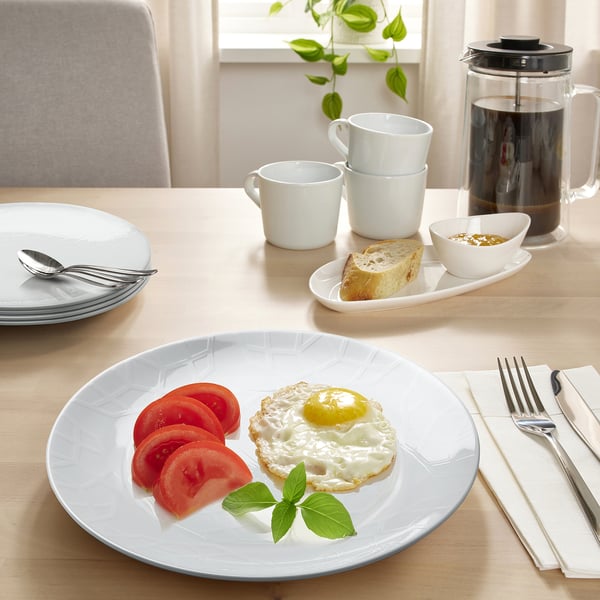 White dinnerware set, including plates, cups, and cutlery, neatly arranged on a table with food.