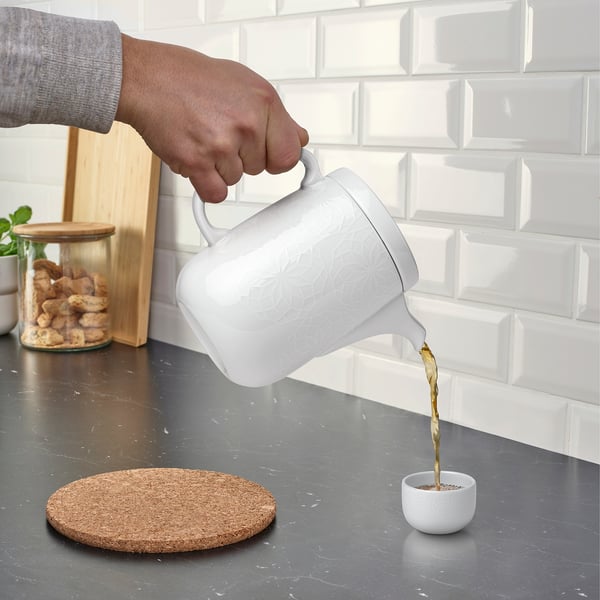 Person pours tea from a white, patterned GOKVÄLLÅ teapot into a small cup on a grey countertop.