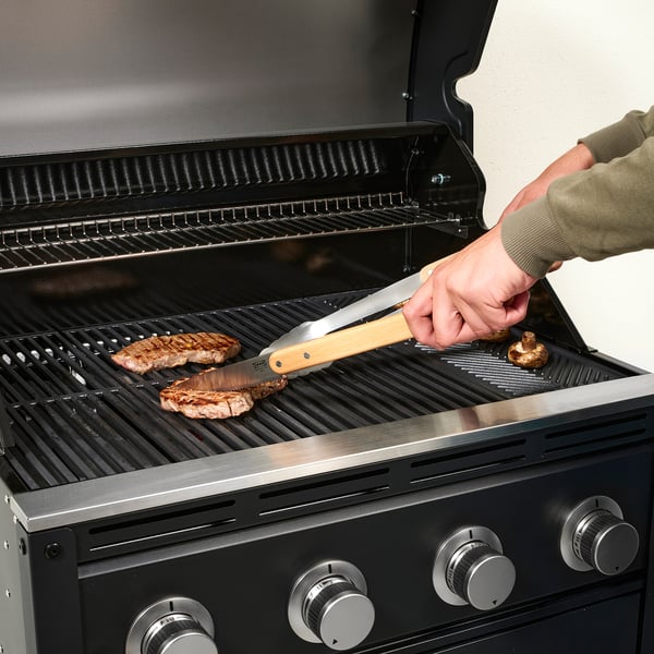 Person grilling steaks and mushrooms using tongs on a gas grill.