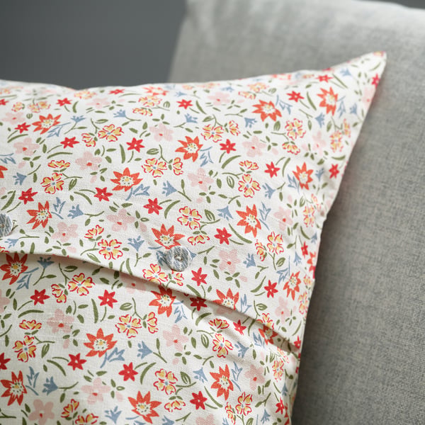 A decorative throw pillow with a delicate floral print rests on a grey cushion. The cover a button closure, bringing a romantic, vintage vibe.