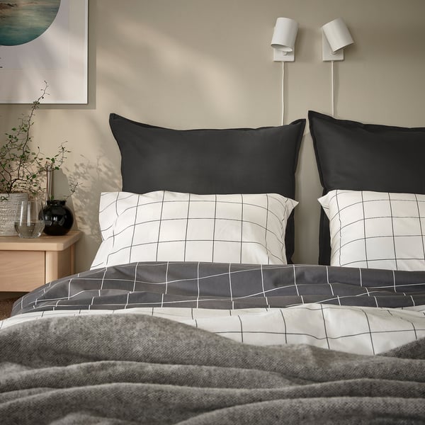 Grey bed with GURLI cushions, white grid patterns, lamps, vase, fleece blanket.