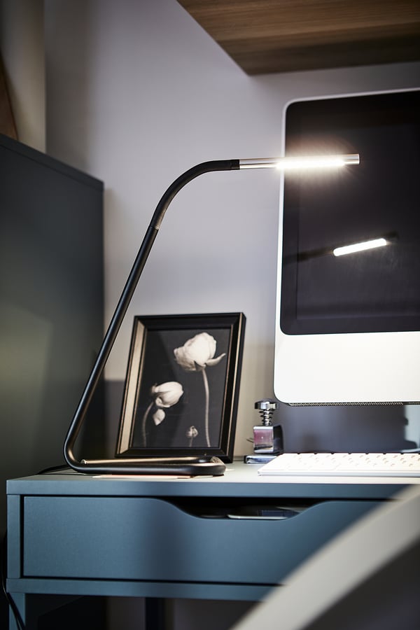 Modern black desk with sleek lamp, monitor, and photo frame.