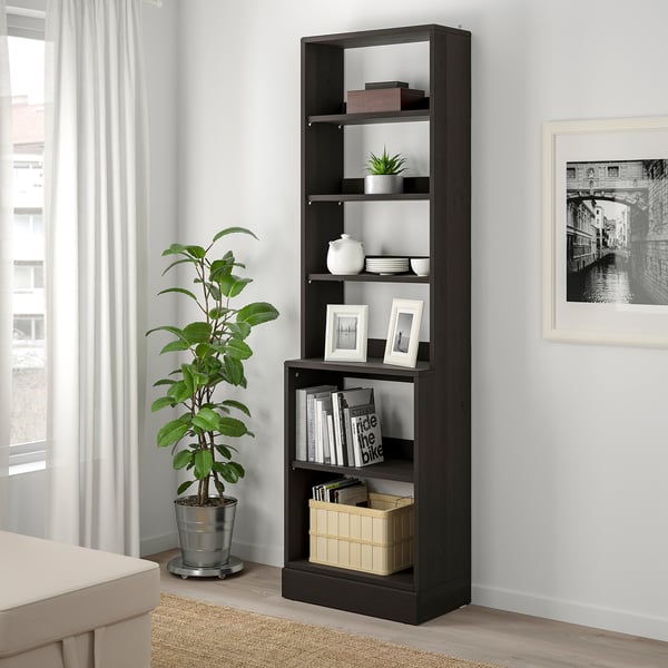 Dark wood HAVSTA shelf by window holds books, vases, pictures.