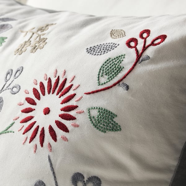 Embroidered cushion with vibrant red and green floral patterns on cream fabric, showcasing high-quality stitching and craftsmanship.