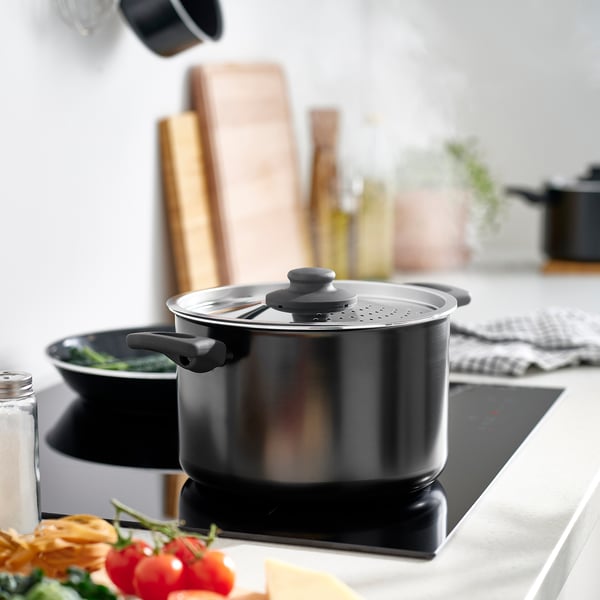 Black saucepan on stove with sturdy handles and large size.