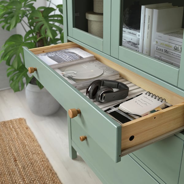 Green cabinet drawer open, revealing headphones, books, and notebooks.