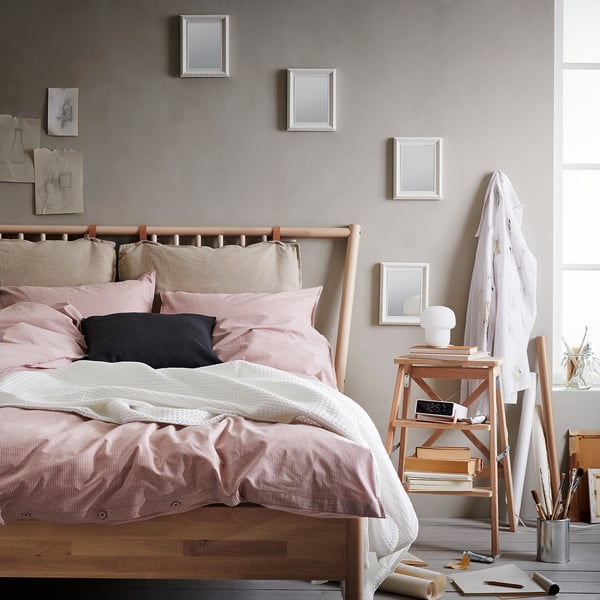 Cosy bedroom with wooden bed, pink pillows, mirrored headboard, side table with lamp, clock, and easel.