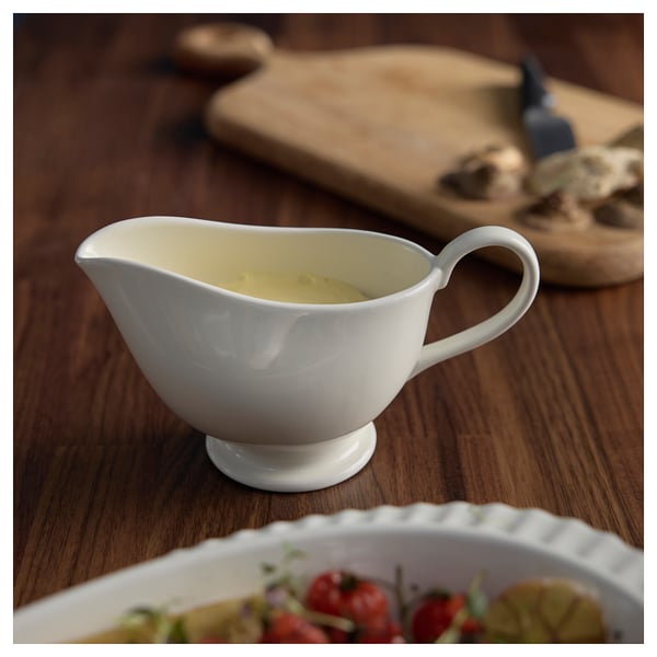 Small white gravy boat with handle holds yellow sauce, sits on wooden table.
