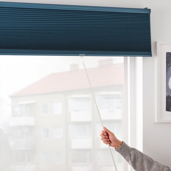 A hand adjusts a dark blue, room-darkening blind, controlling light and providing privacy. The blind has a hidden, safe cord for child protection.