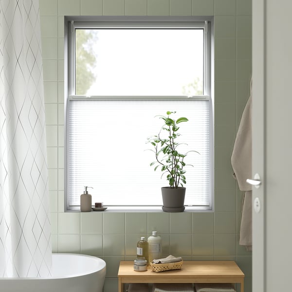Modern bathroom with wide window, HORNVALLMO blind, plant, towels, green tiles.