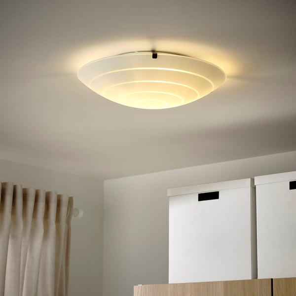 A softly lit, frosted glass ceiling lamp hangs from an off-white ceiling, brightness evenly diffused for room illumination.