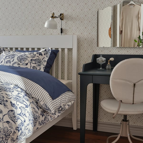 Bedroom with IDANÄS white bed, blue linens, wall sconce, mirror, vanity, and chair.