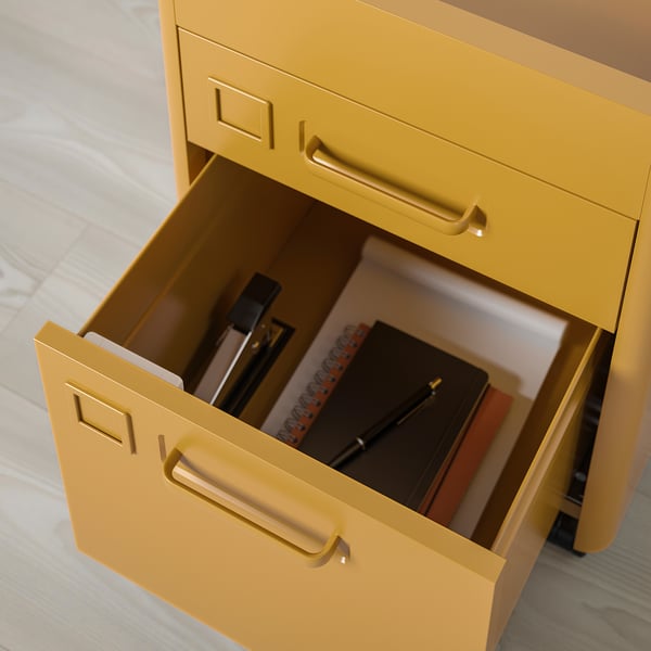 Bright yellow drawer unit with gold handles, one drawer open showing journals and writing tools.