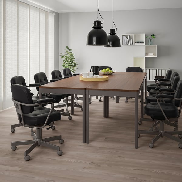 Modern office with IDÅSEN tables and black chairs, pendant lamps, greenery, and fruit tray.