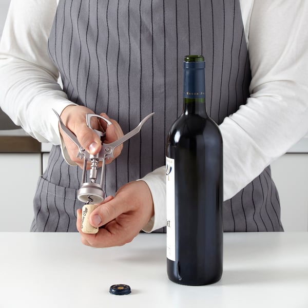 Person uses corkscrew tool to open wine bottle, with levers for easy uncorking.