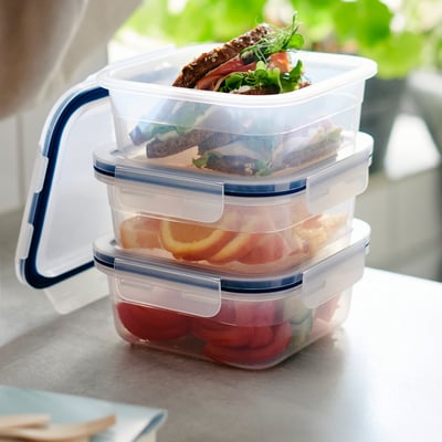 Stacked clear food containers with blue lids, showing meals, on countertop.